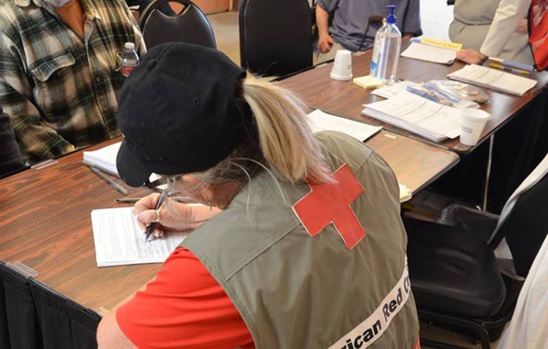 Red Cross volunteer filling out paperwork at table with other people sitting at table.