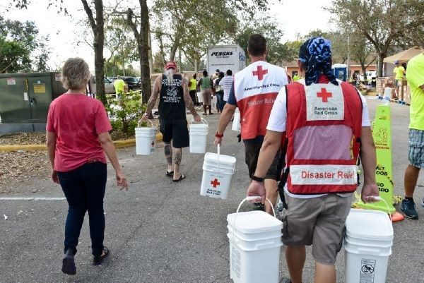 Red Cross volunteers carrying buckets in each hand.