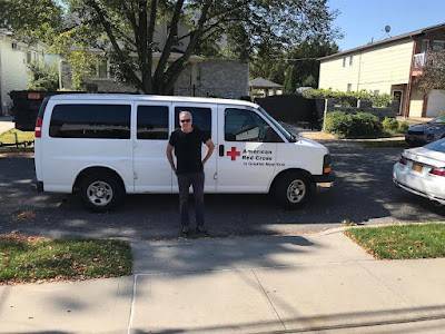 Red Cross volunteer wearing sunglasses standing next to Red Cross van in street.