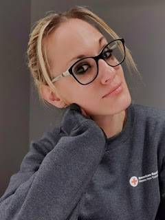 Red Cross volunteer wearing glasses and a Red Cross sweater takes a selfie.