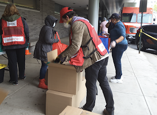 Red Cross volunteers wearing masks and moving boxes that are outside of a building.