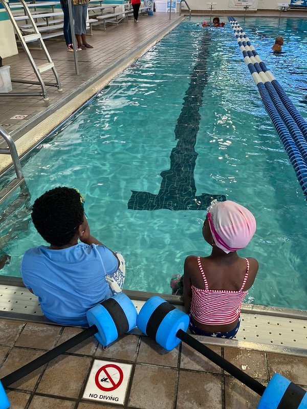 two children sitting at end of pool.