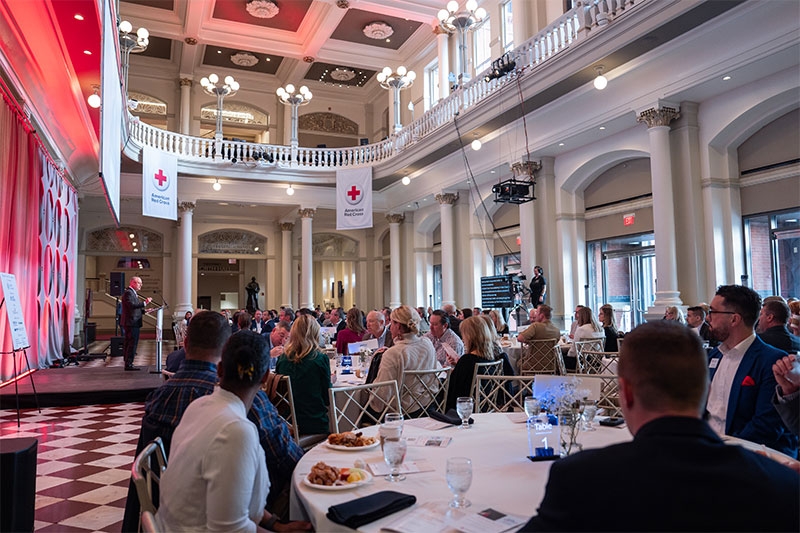 Red Cross Clara Barton event with room full tables, people, and a speaker on stage.