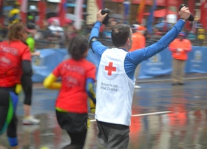 Marathon runner in race with American Red Cross logo on back of shirt, raising arms.